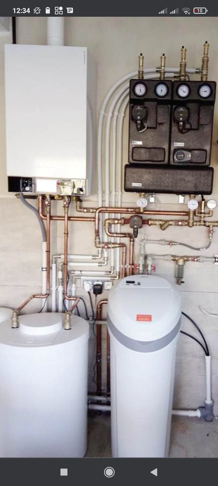 Nowoczesny, wiszący piec centralnego ogrzewania z rozbudowaną instalacją hydrauliczną, manometrami i dwoma zbiornikami, zainstalowany w pomieszczeniu technicznym.