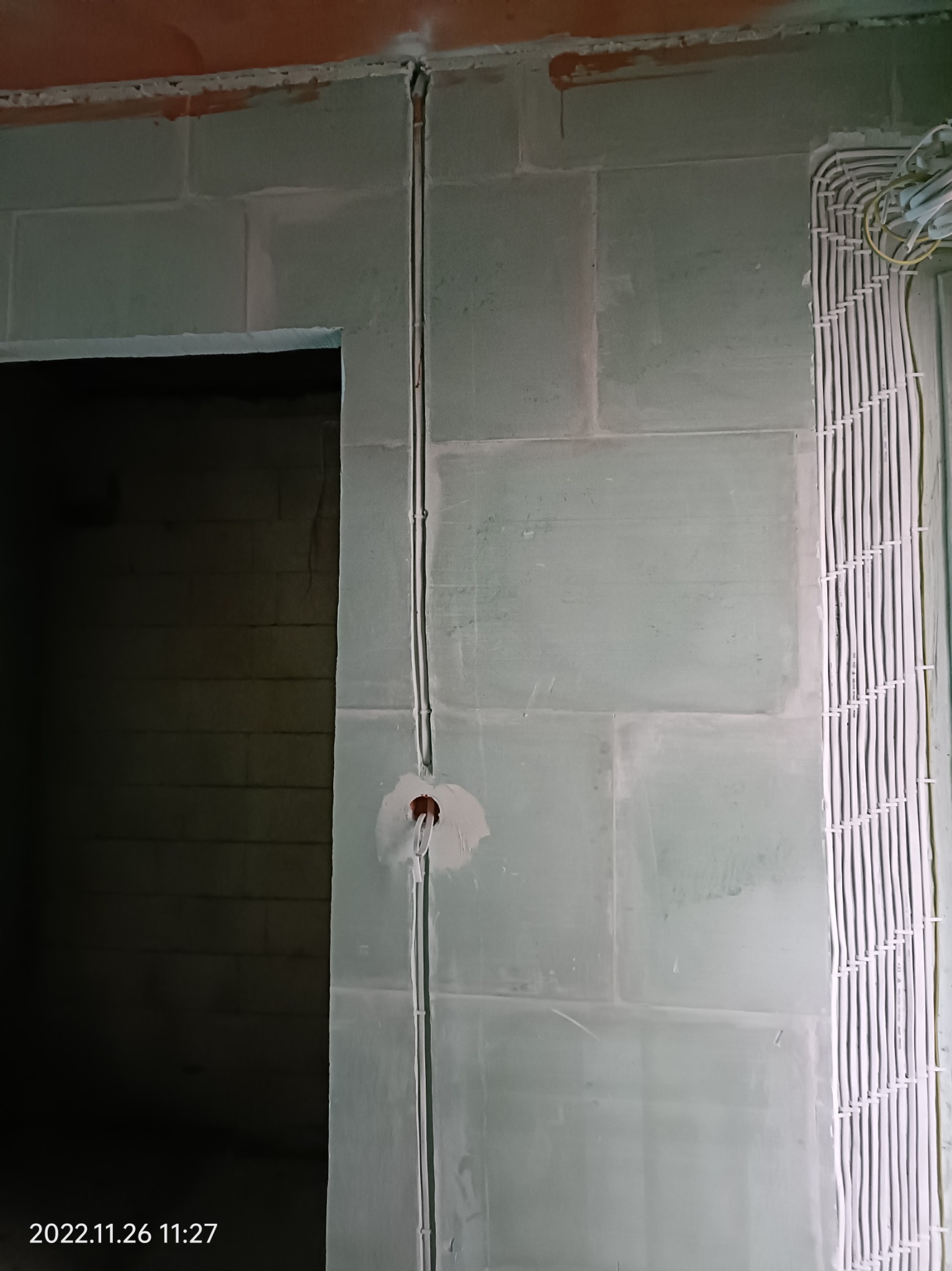 Wewnętrzna ściana z pustaków z pionowo poprowadzonym przewodem elektrycznym w peszlu i otworem pod gniazdko, obok widoczna wiązka kabli ułożona w korytku.