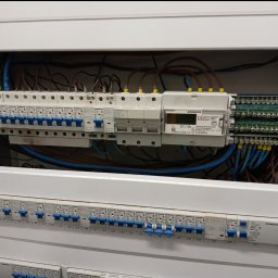 ElektroComplex - Rozdzielnica elektryczna Schrack z zamontowanymi bezpiecznikami i licznikiem energii elektrycznej, widoczne przewody i oznaczenia.