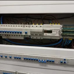 Rozdzielnica elektryczna Schrack z zamontowanymi bezpiecznikami i licznikiem energii elektrycznej, widoczne przewody i oznaczenia.