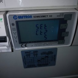 ElektroComplex - Szczegółowe ujęcie inteligentnego licznika energii Eastron SDM630MCT V2, zamontowanego w szarej skrzynce, z widocznym schematem połączeń i napisem 'SMART METER INST PV' nad nim.