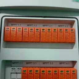 Rozdzielnica fotowoltaiczna z zabezpieczeniami przepięciowymi VCX dla różnych MPPT, widoczne bezpieczniki i moduły ochrony przepięciowej w obudowie.