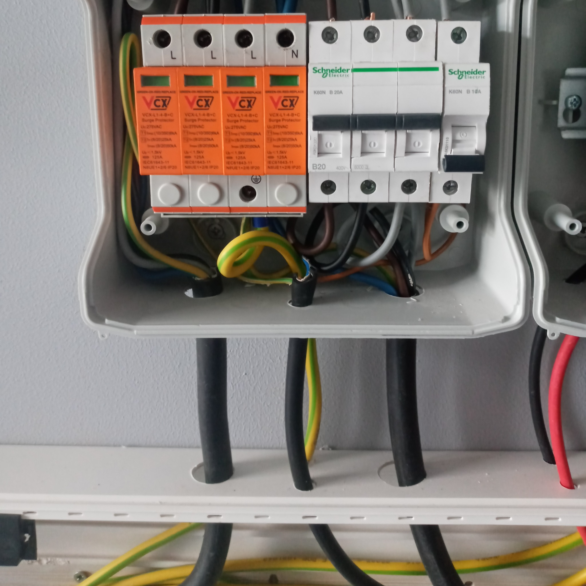 Rozdzielnia elektryczna z zamontowanymi ogranicznikami przepięć VCX i wyłącznikami nadprądowymi Schneider Electric, widoczne przewody w różnych kolorach.