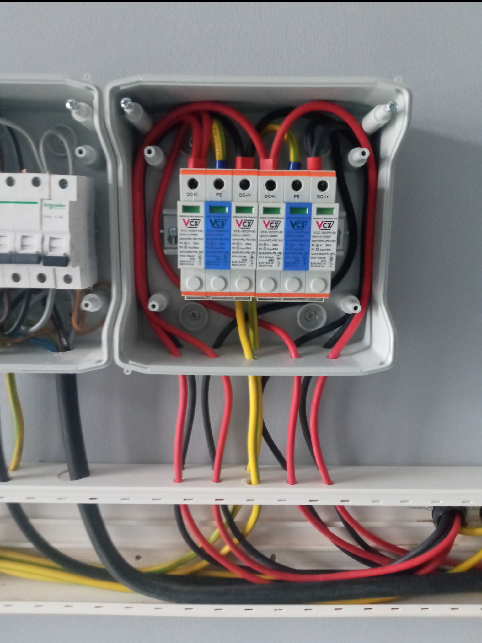 Rozdzielnica fotowoltaiczna z zabezpieczeniami przepięciowymi VCX 1000PV40 i wyłącznikiem Schneider, widoczne kable czerwone, czarne i żółto-zielone.