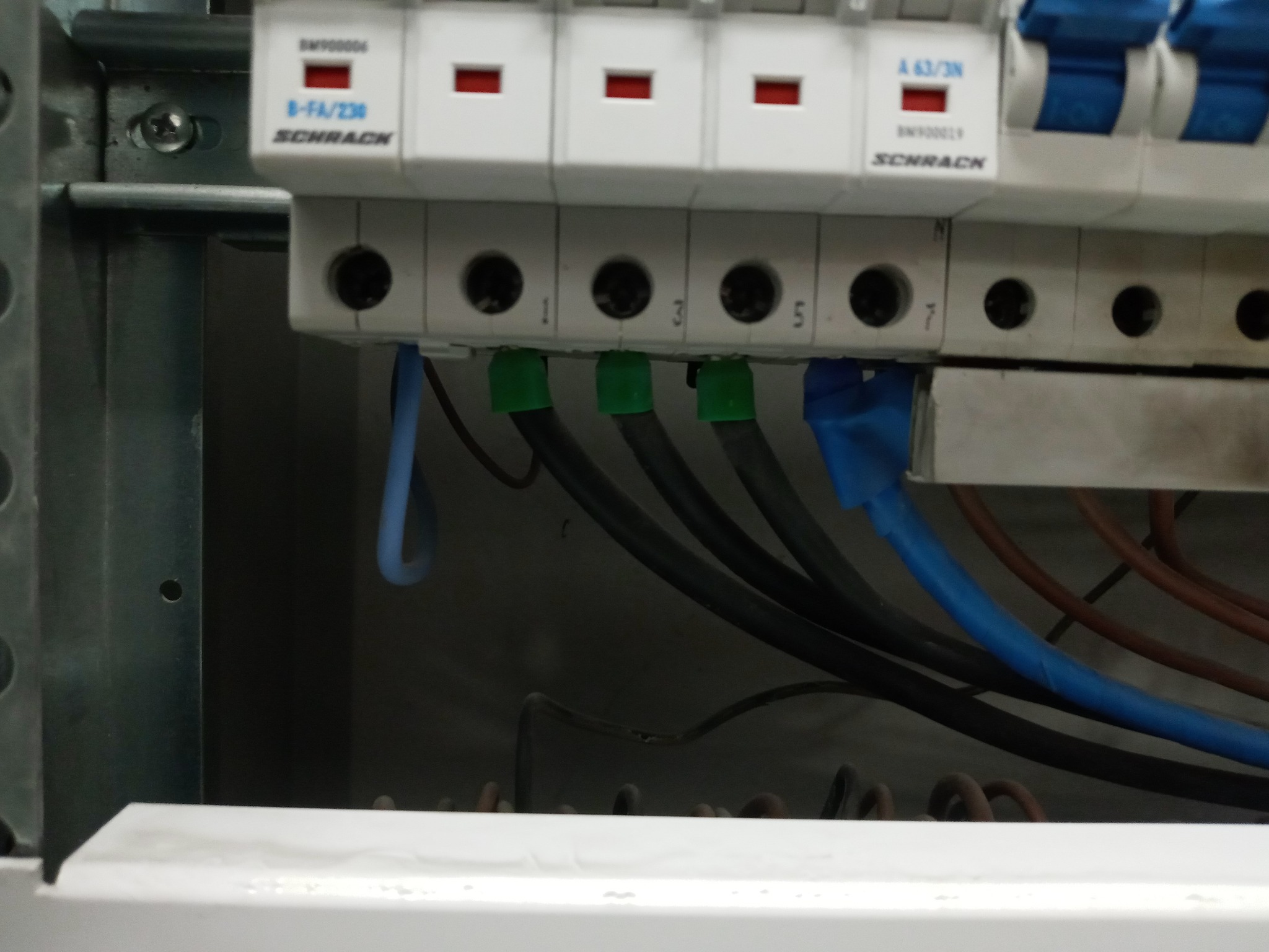 Szczegółowe ujęcie podłączenia przewodów do listwy zaciskowej w rozdzielnicy elektrycznej, widoczne oznaczenia numerów na listwie i kolorowe izolacje przewodów.