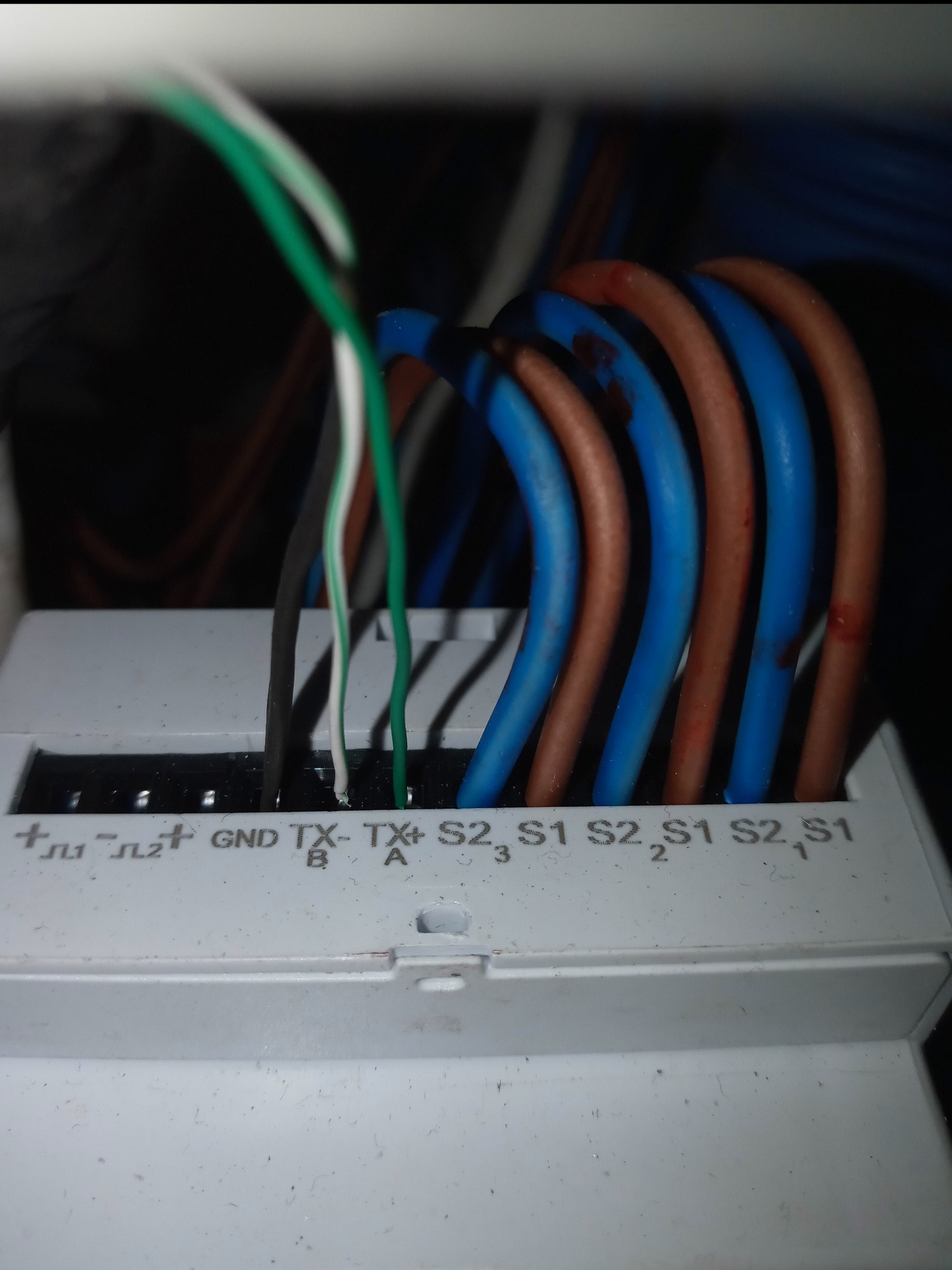 Zbliżenie na podłączenie przewodów: zielony, biały, czarny do złącz TX-A, TX-B, GND w białej skrzynce, obok przewody niebieskie i brązowe podłączone do S1 i S2.
