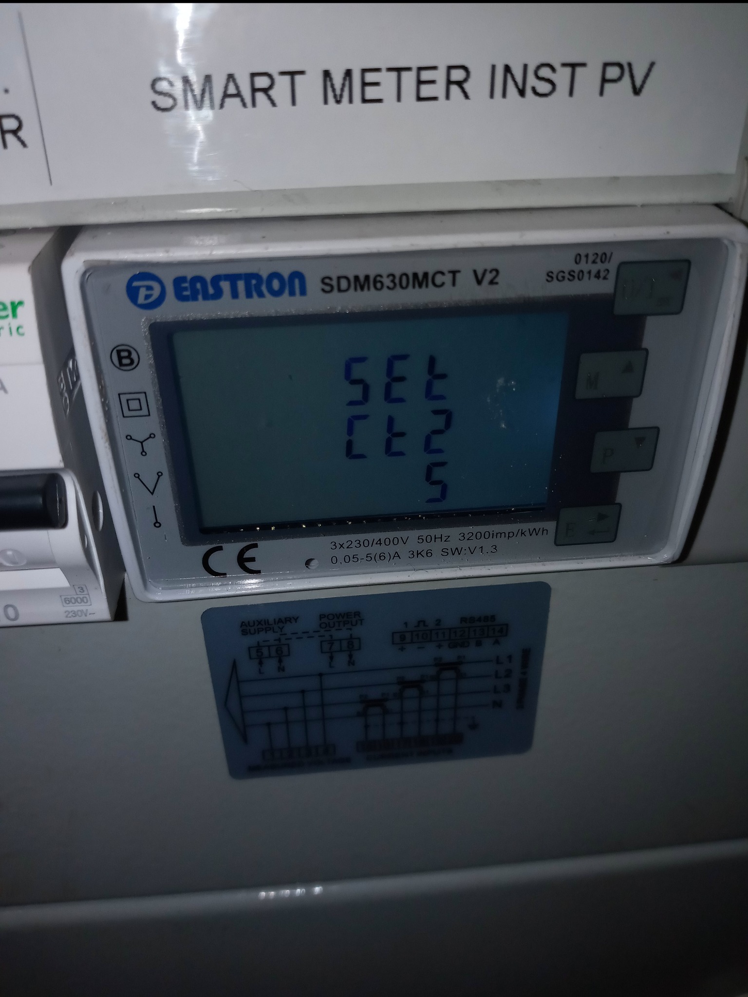 Szczegółowe ujęcie inteligentnego licznika energii Eastron SDM630MCT V2, zamontowanego w szarej skrzynce, z widocznym schematem połączeń i napisem 'SMART METER INST PV' nad nim.