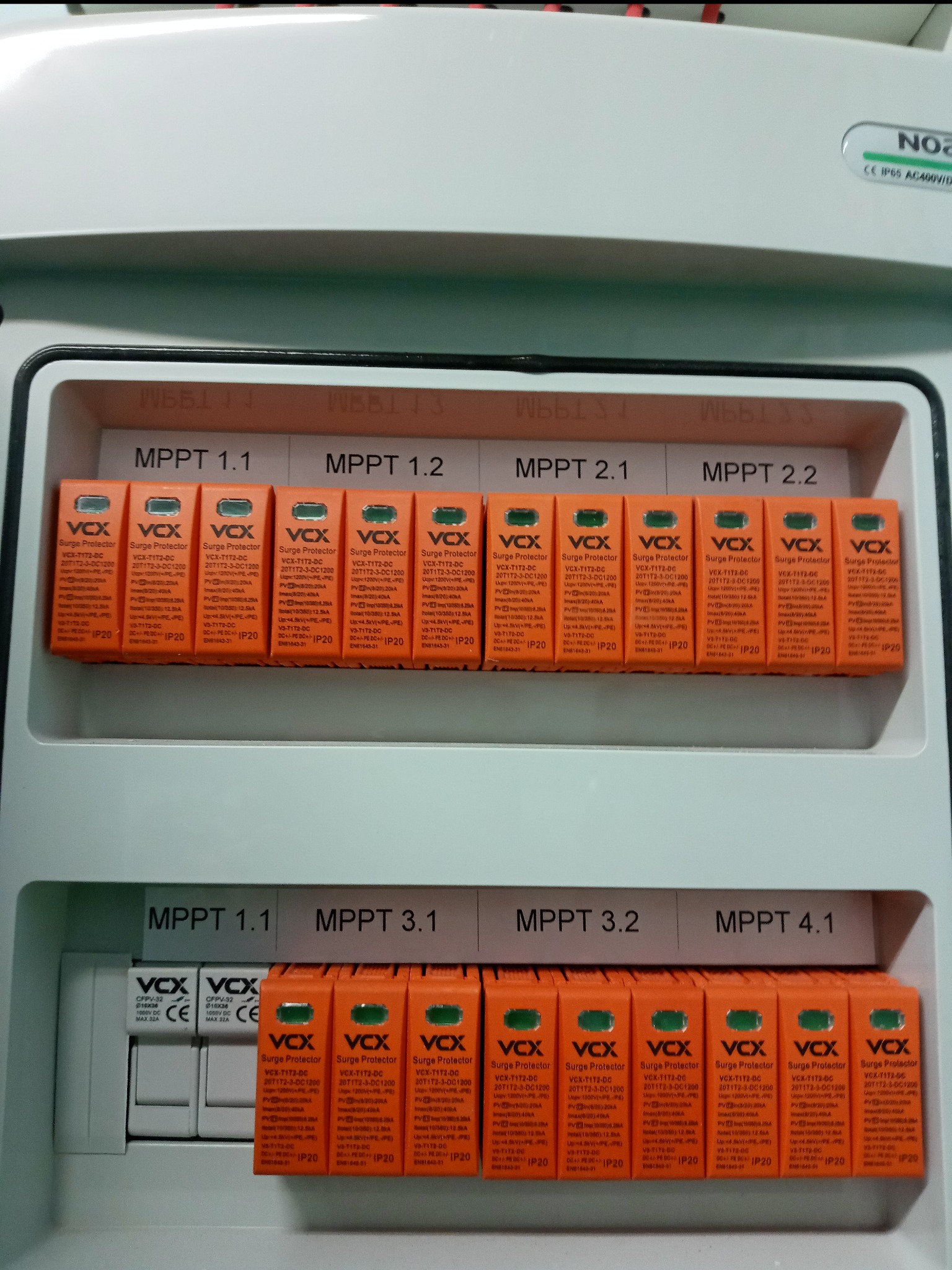 Rozdzielnica fotowoltaiczna z zabezpieczeniami przepięciowymi VCX dla różnych MPPT, widoczne bezpieczniki i moduły ochrony przepięciowej w obudowie.