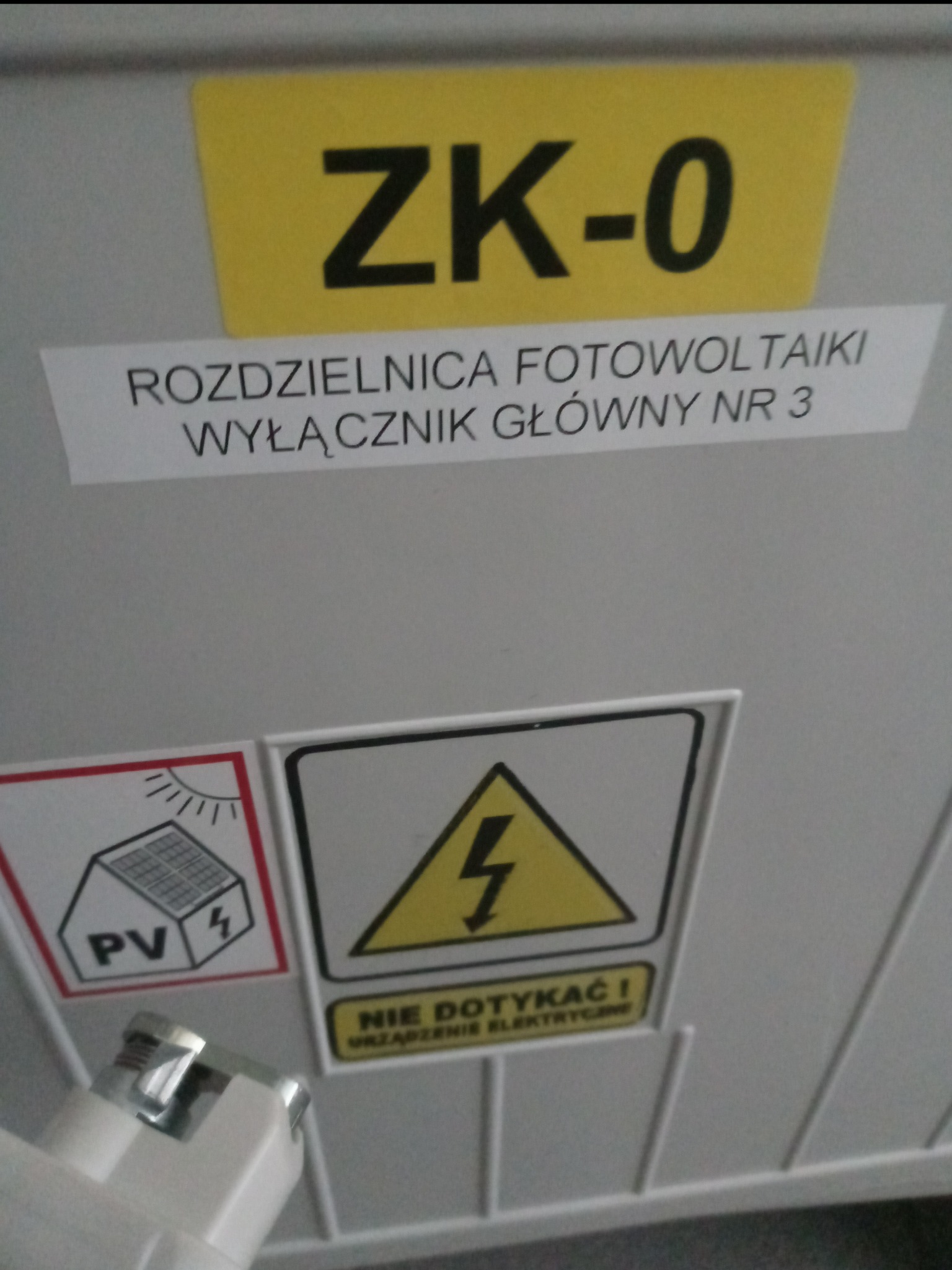 Oznakowana rozdzielnica fotowoltaiki z wyłącznikiem głównym nr 3, ostrzeżenie przed porażeniem elektrycznym i schemat instalacji PV.