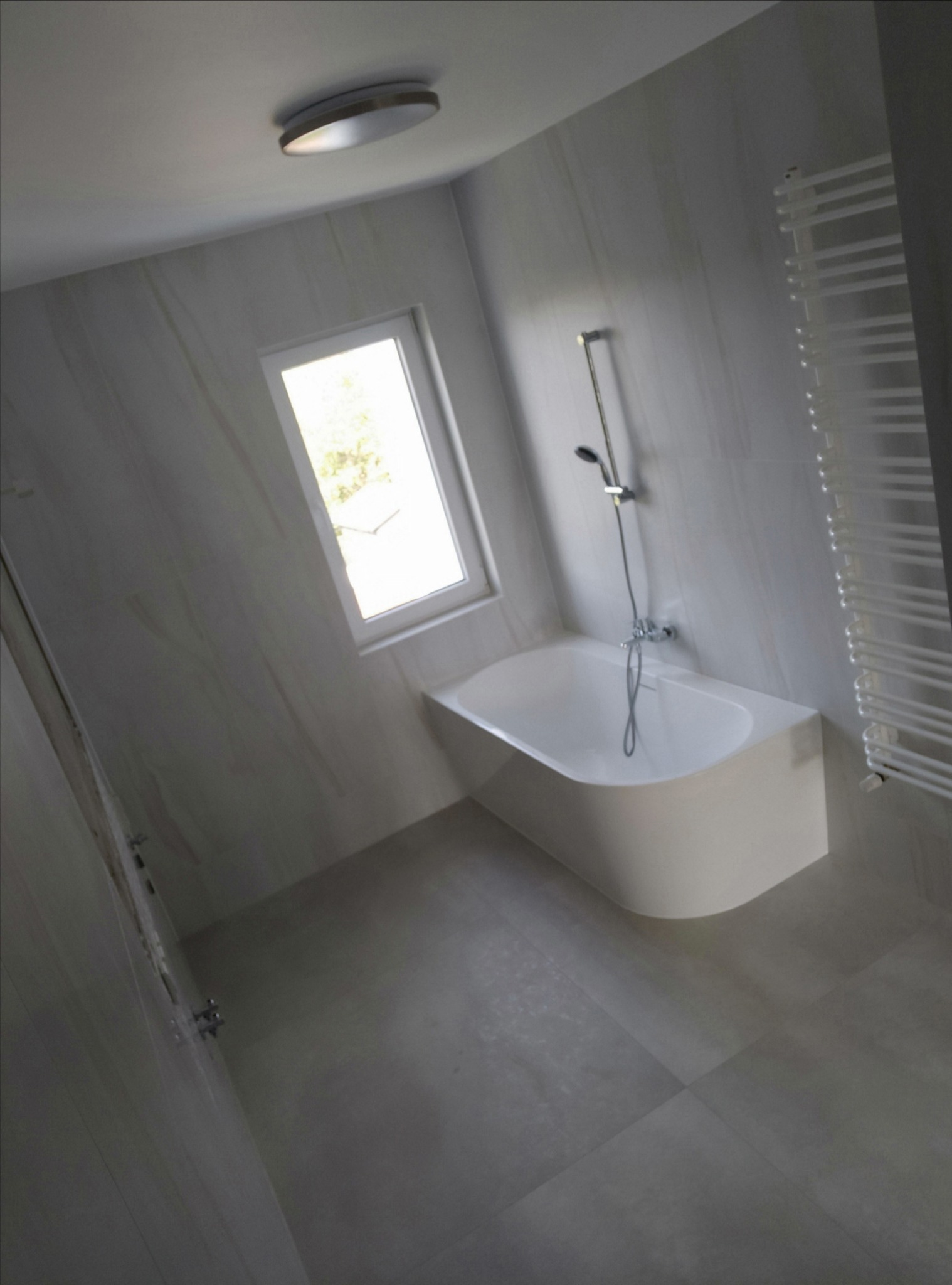 Wykończona łazienka w odcieniach szarości z wanną przy oknie, grzejnikiem drabinkowym i punktowym oświetleniem sufitowym.