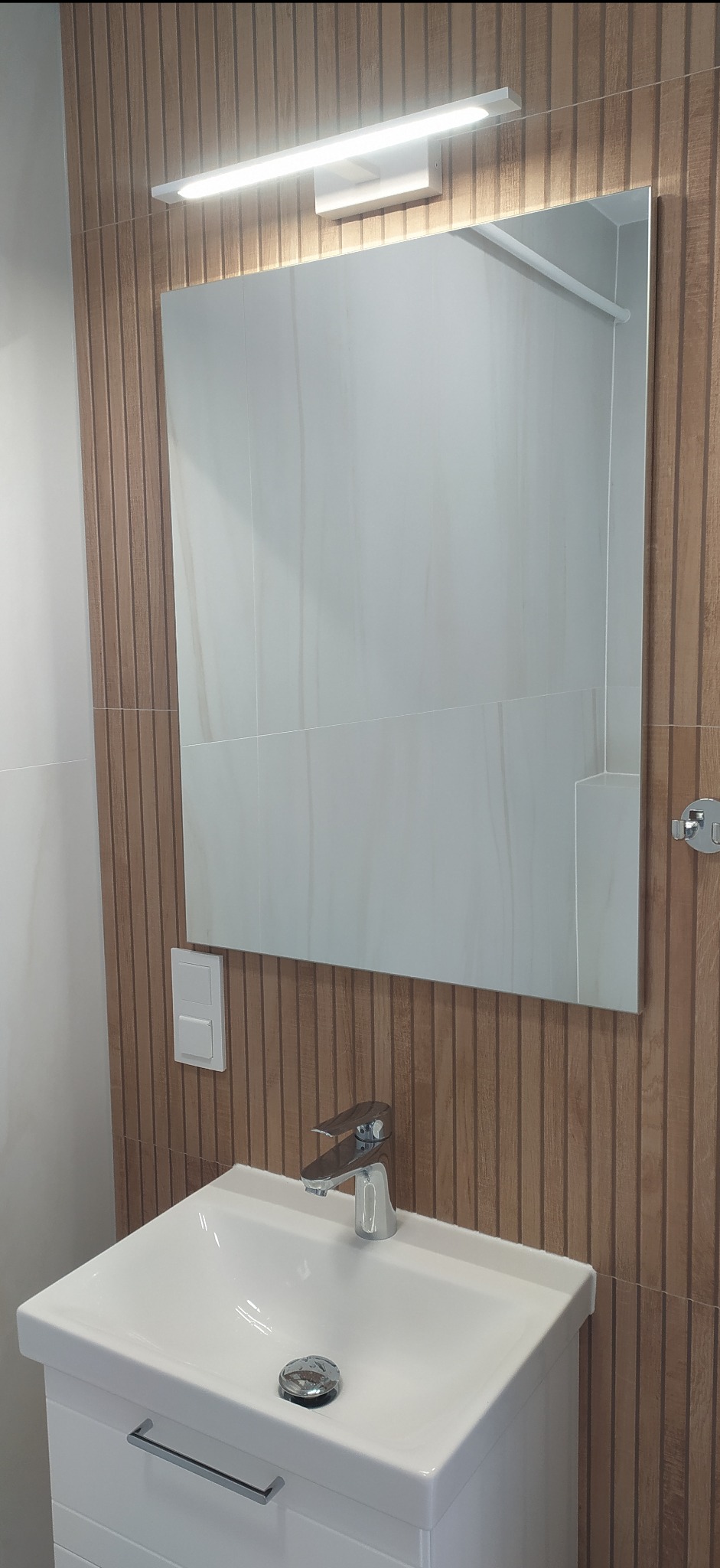Nowoczesna łazienka z umywalką nablatową, lustrem z oświetleniem LED i ścianą wykończoną panelami imitującymi drewno.