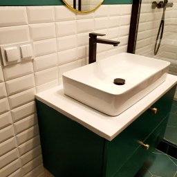 Ergonomic Marta Szponarska - Nowoczesna łazienka z białą, prostokątną umywalką nablatową, czarną armaturą i zieloną szafką z złotymi uchwytami na tle białych, trójwymiarowych płytek ściennych i heksagonalnych płytek podłogowych.