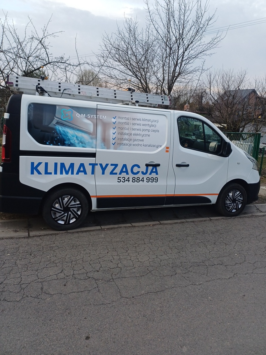 Biały samochód dostawczy z niebieskim napisem 'KLIMATYZACJA' i numerem telefonu, na dachu drabina, reklama usług montażu i serwisu klimatyzacji, wentylacji i pomp ciepła.
