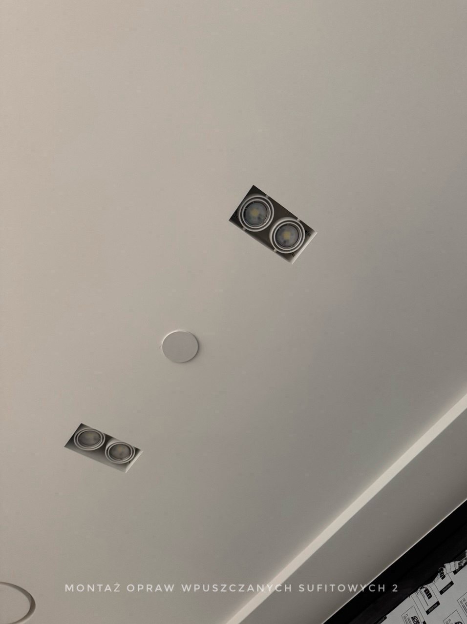 Sufit podwieszany z trzema otworami na oświetlenie w Krakowie: dwa prostokątne z podwójnymi lampami LED i jeden okrągły, widok od dołu.