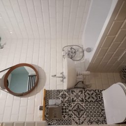 fteshhousejremonty - Białe, podłużne płytki na ścianie łazienki, dekoracyjne płytki pod umywalką i toaletą, okrągłe lustro z lampą, bateria umywalkowa w stylu retro.