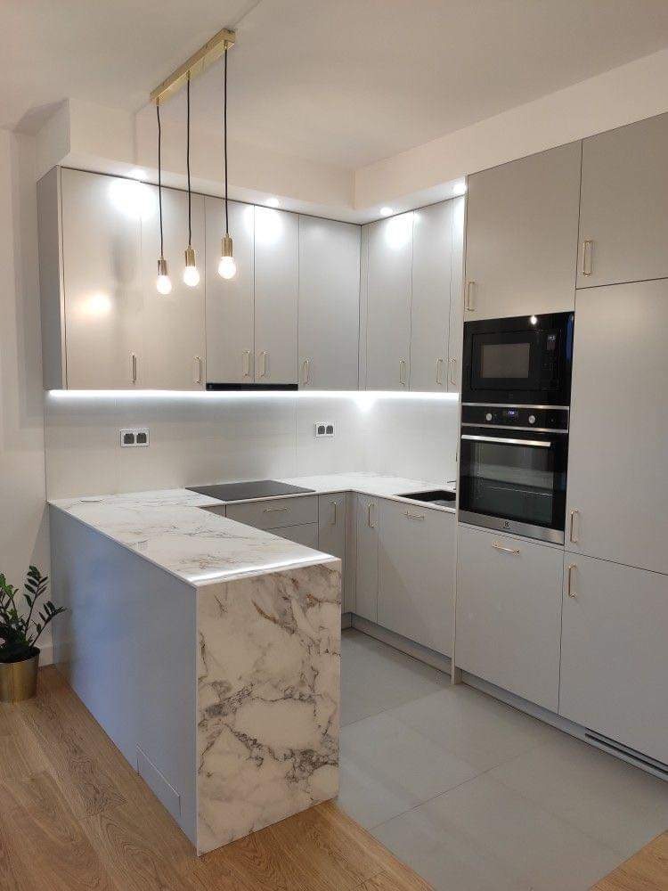 Nowoczesna kuchnia z szarymi, lakierowanymi frontami, marmurowym blatem wyspy i złotymi lampami wiszącymi nad nią.