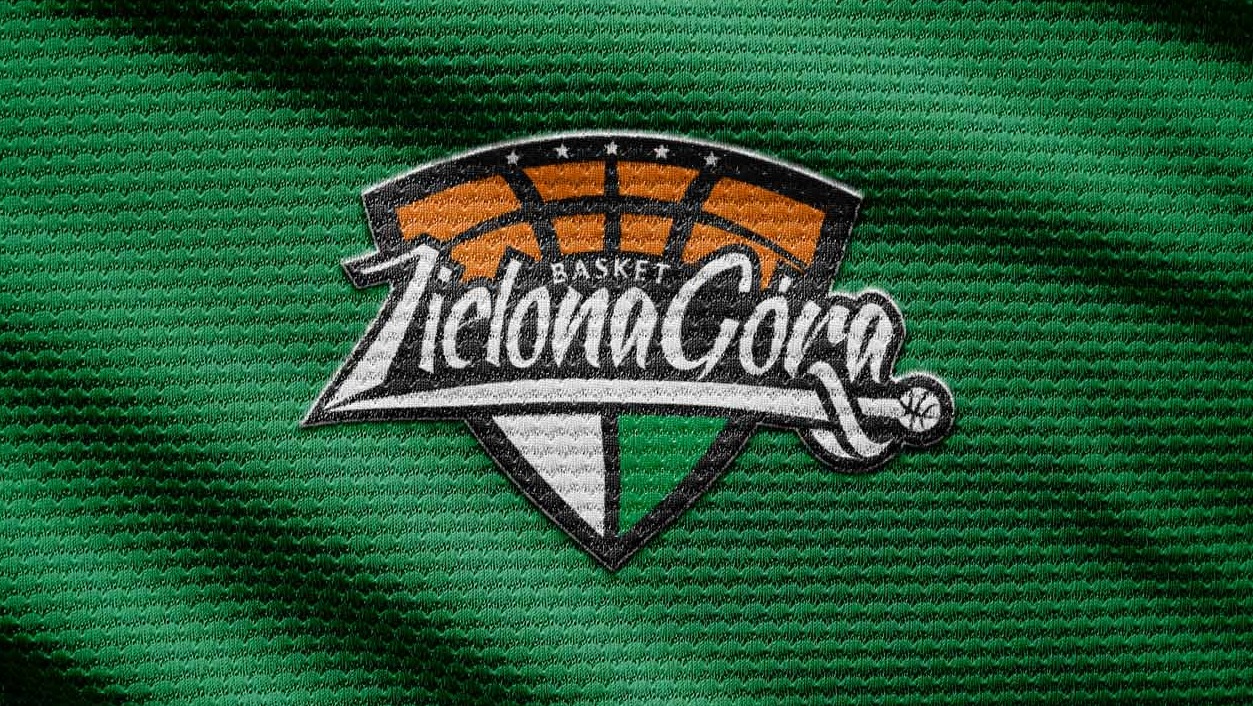 Wyhaftowane logo drużyny koszykarskiej 'Zelona Góra' na zielonej, teksturowanej tkaninie. Logo zawiera elementy graficzne takie jak kosz, piłka i gwiazdy.