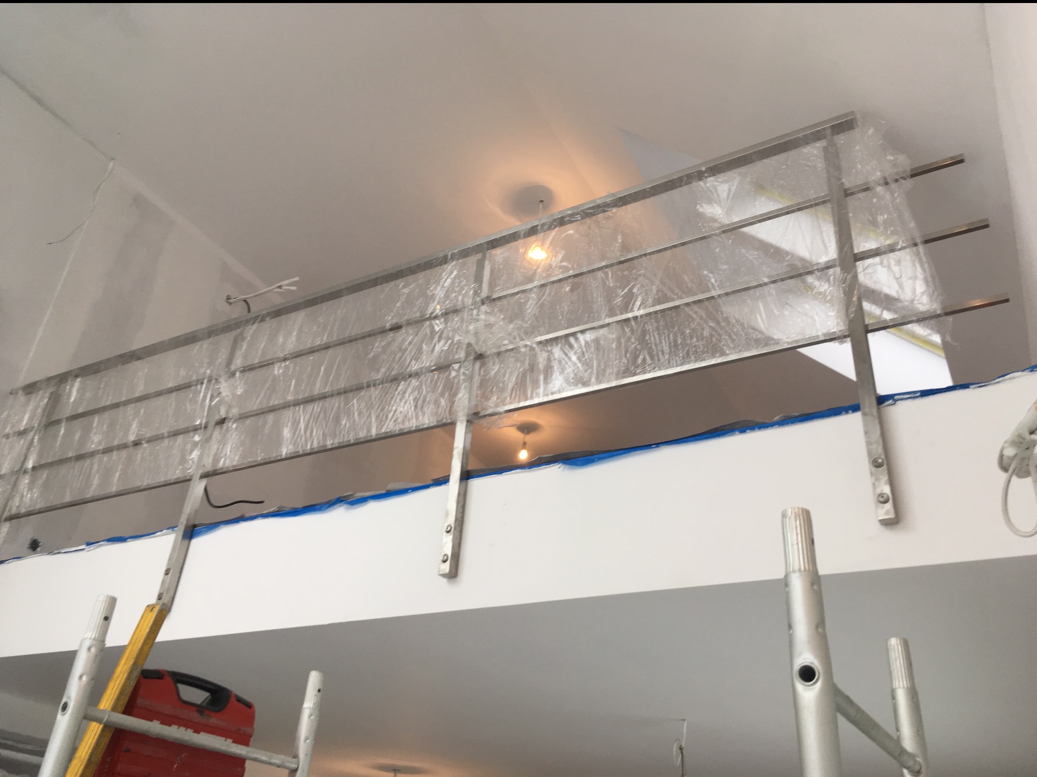 Nierdzewna balustrada na antresoli, zabezpieczona folią ochronną podczas prac wykończeniowych. Widoczny fragment drabiny i skrzynki narzędziowej.