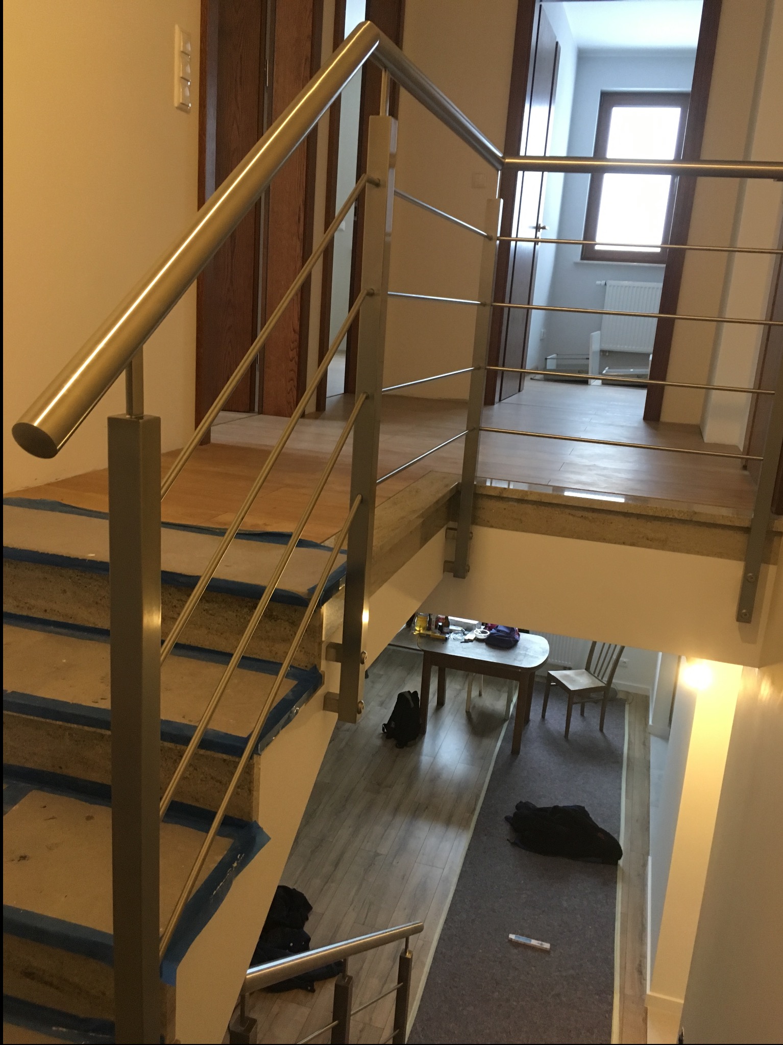 Nowoczesna balustrada nierdzewna z poziomymi prętami na schodach w domu we Wrocławiu. Schody zabezpieczone taśmą malarską, widok z góry na niższy poziom.