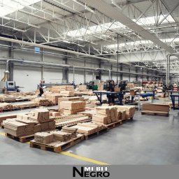 VIA VOX GROUP SPÓŁKA AKCYJNA - Wnętrze hali produkcyjnej z przygotowanym drewnem na paletach, widoczny pracownik w oddali i maszyny do obróbki drewna.