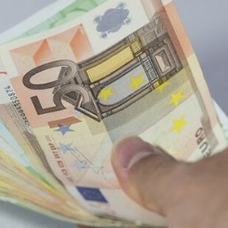 MONIKA FINANSE - Dłoń trzymająca plik banknotów euro (100 i 50) na tle kalkulatora.