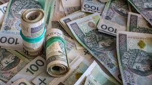 Stosy i rozrzucone banknoty 100-złotowe, zabezpieczone gumkami recepturkami, tworzące wrażenie obfitości finansowej.