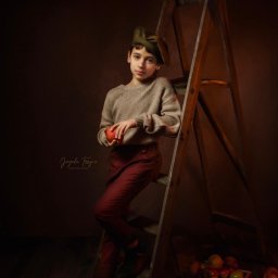 Jagoda Trzyna Photography - Portret chłopca w zielonej czapce, opartego o drewnianą drabinę, trzymającego czerwone jabłko na tle ciemnego studia z skrzynką pełną jabłek w dolnym rogu.