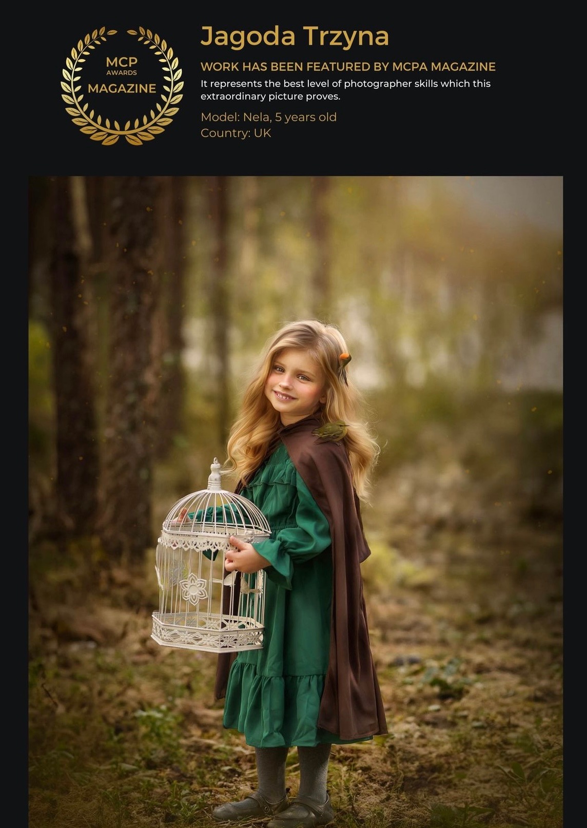 Portret uśmiechniętej, pięcioletniej dziewczynki o blond włosach w zielonej sukience i brązowej pelerynie, trzymającej ozdobną, białą klatkę dla ptaków na tle leśnym.