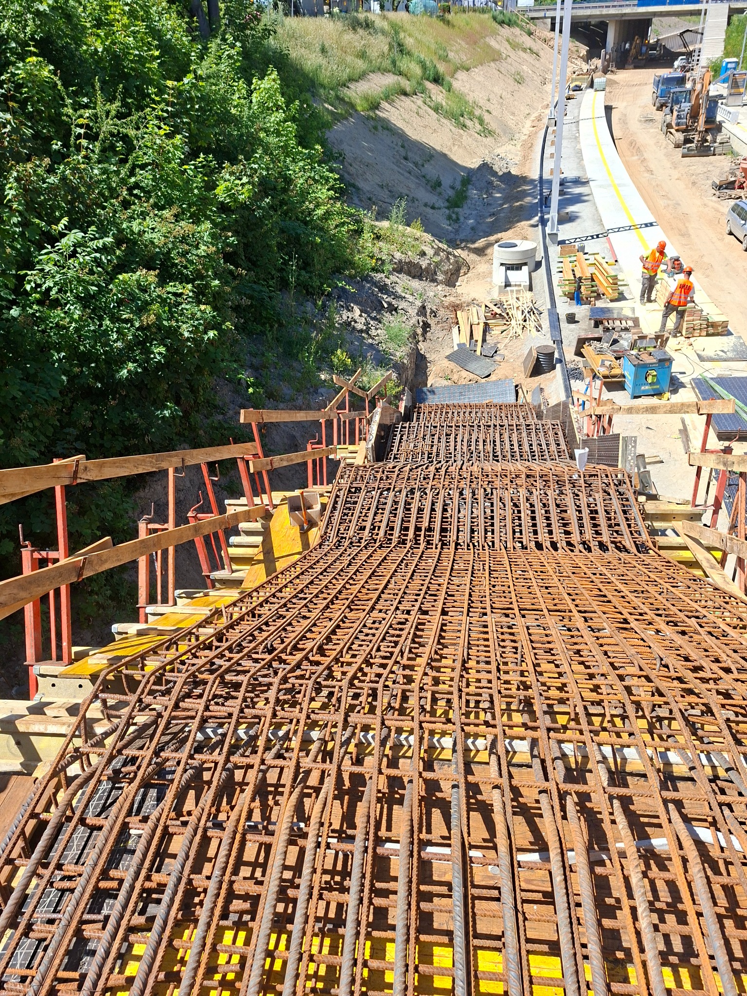 Skomplikowane zbrojenie podłoża z widoczną konstrukcją szalunkową i pracownikami w tle. Budowa drogi z perspektywy z góry w słoneczny dzień.