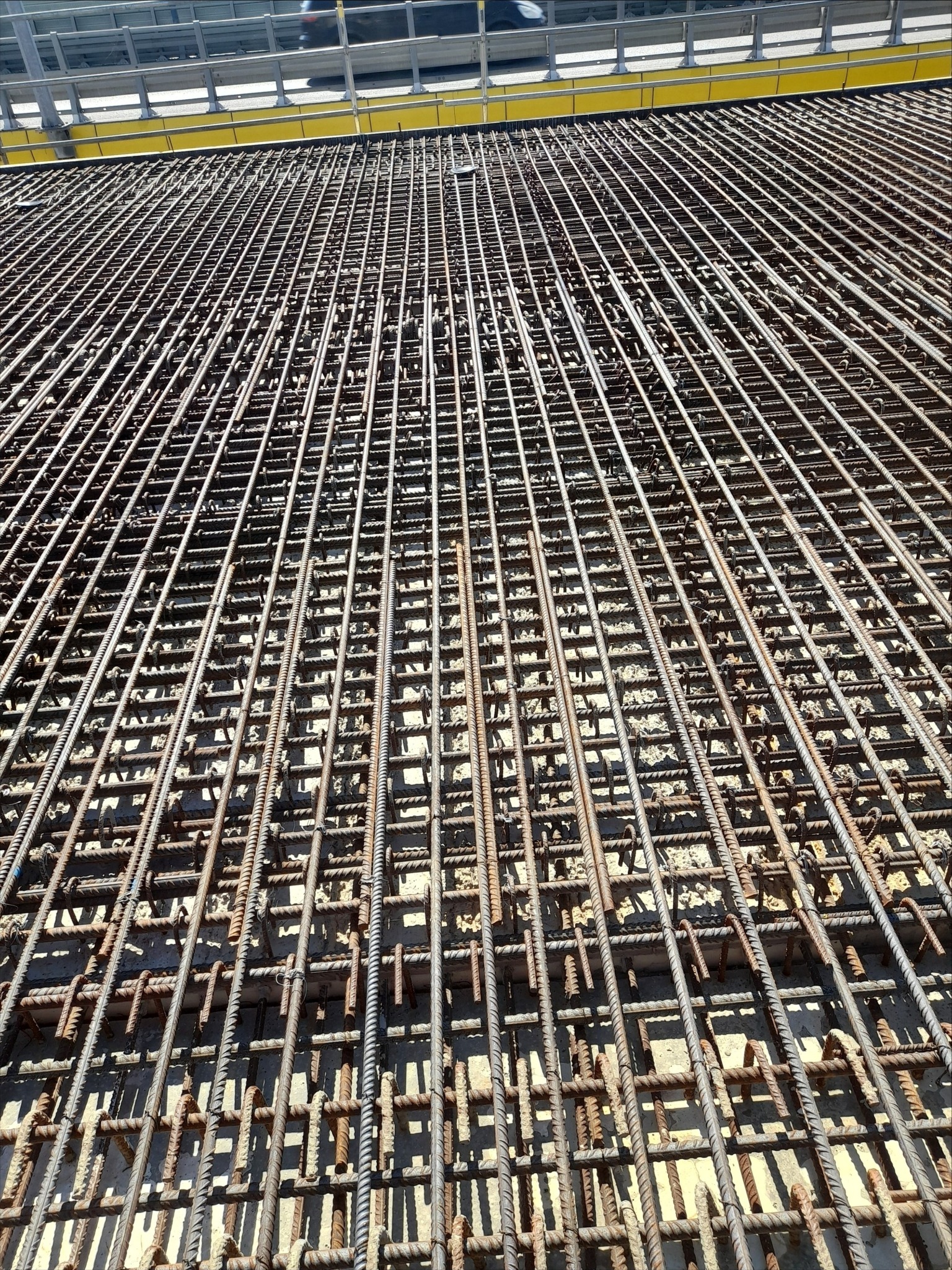 Siatka z prętów żebrowanych, tworząca zbrojenie fundamentu. Widok z góry, regularny układ, szare pręty na jasnym podłożu. Element konstrukcyjny przed betonowaniem.