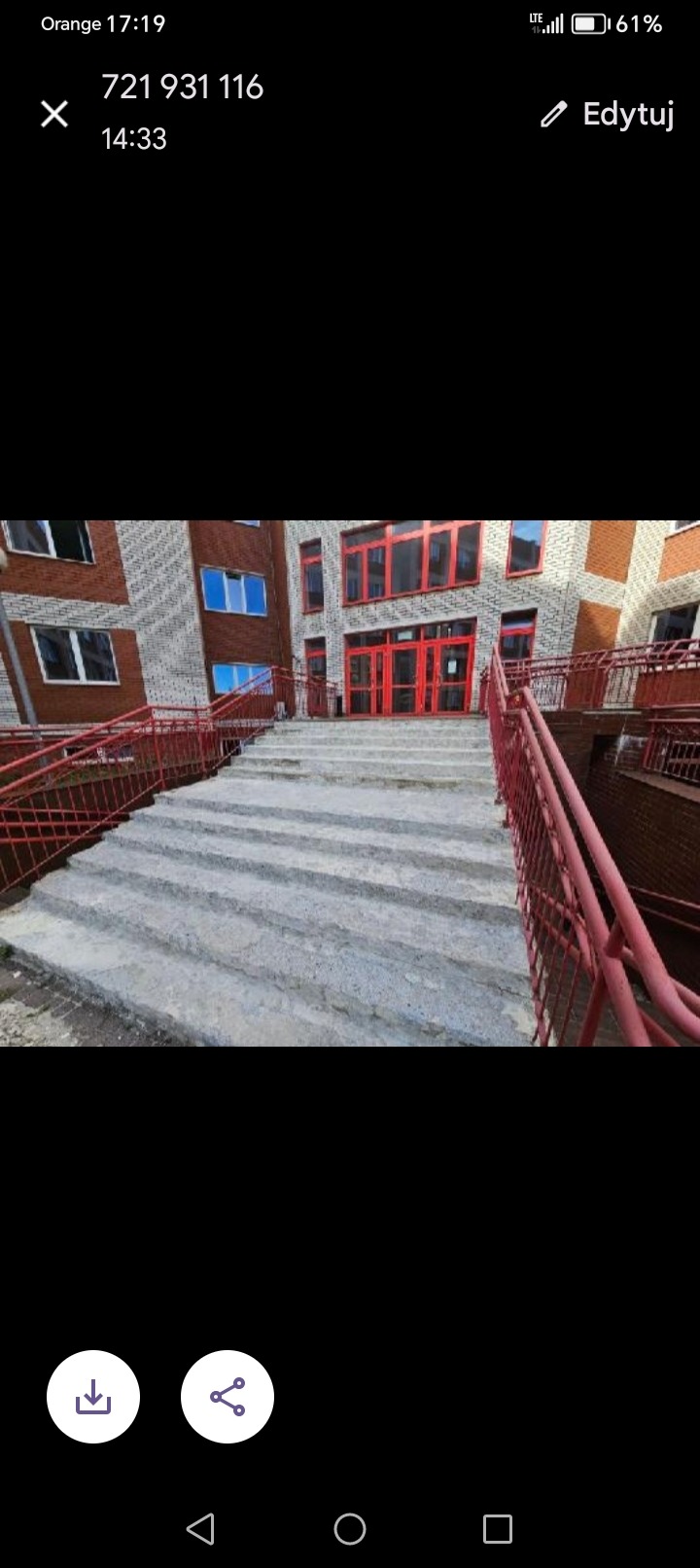 Betonowe schody wejściowe do budynku z czerwonymi barierkami i stolarką okienną, widoczne nierówności powierzchni betonu.