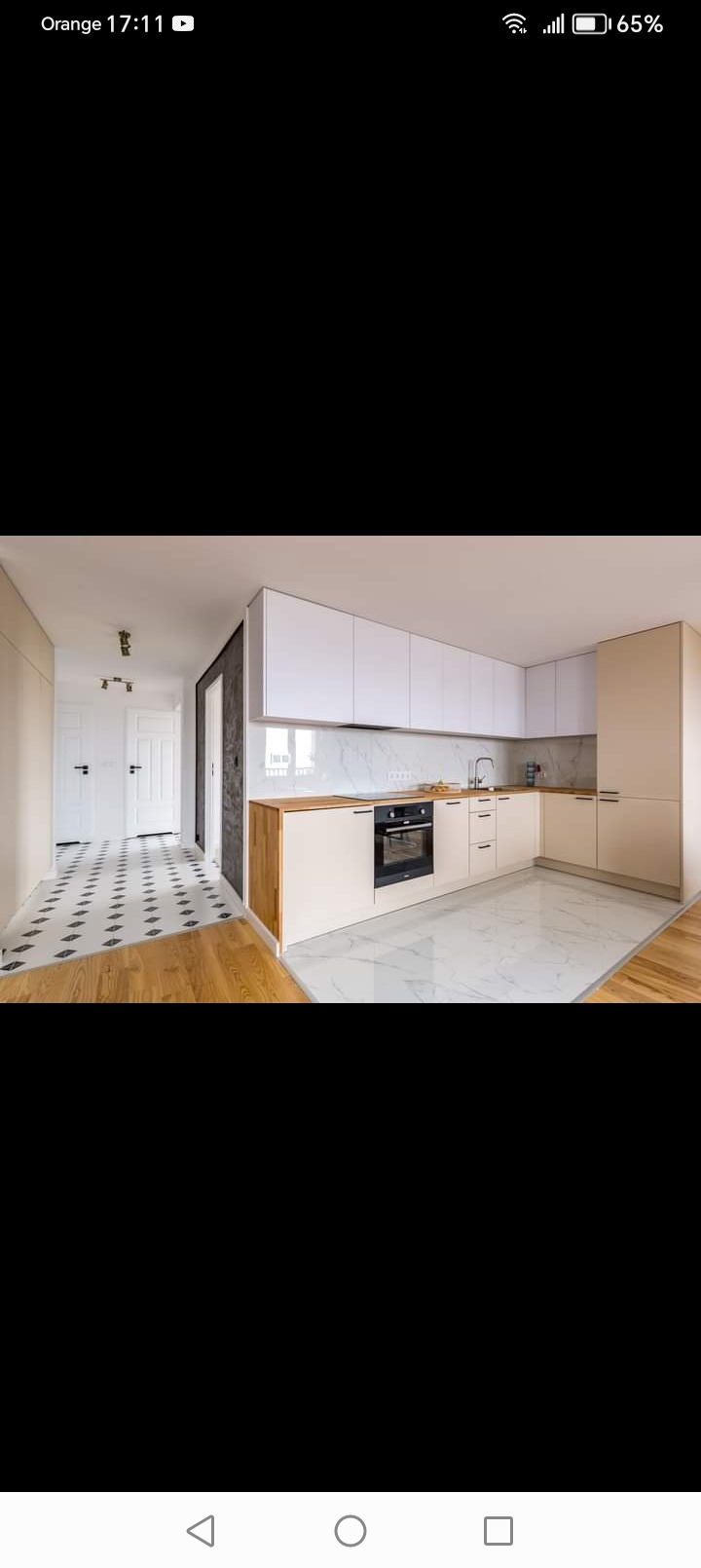 Nowoczesna kuchnia w odcieniach bieli i beżu z marmurowym blatem i podłogą, widok na korytarz z biało-czarną podłogą.