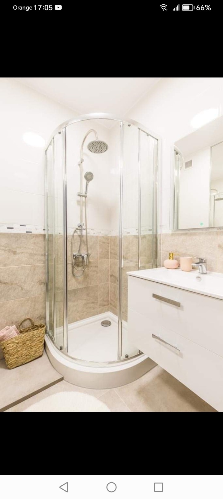 Nowoczesna łazienka z narożną kabiną prysznicową z chromowanymi detalami, białą szafką umywalkową i wiklinowym koszem na ręczniki.