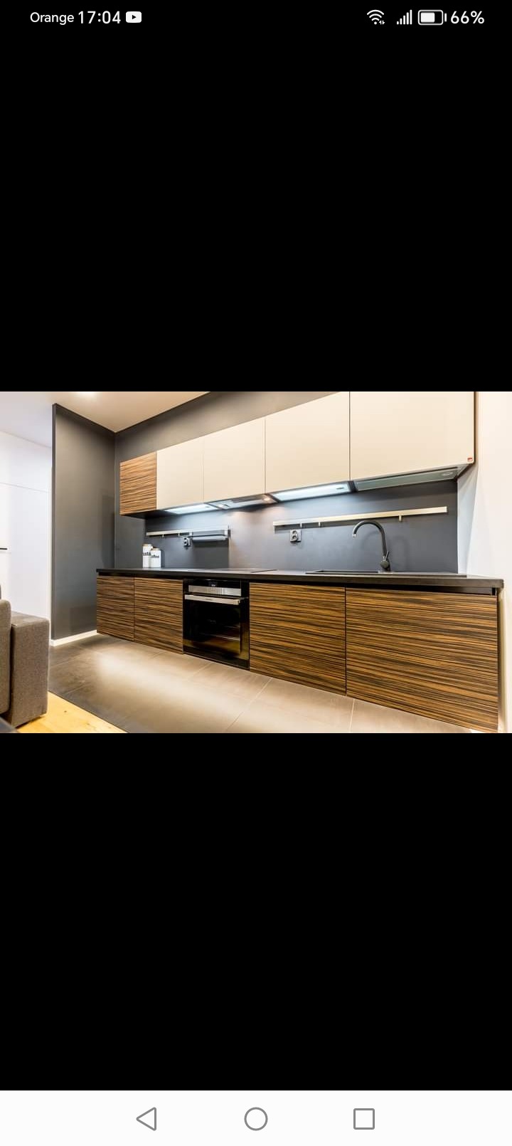 Nowoczesna kuchnia z frontami szafek w kolorze ciemnego drewna, jasnymi szafkami wiszącymi i czarnym blatem, oświetlona punktowymi lampami podszafkowymi.