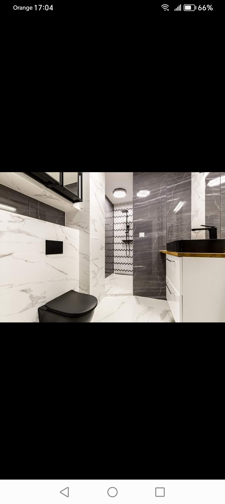 Nowoczesna łazienka z czarną armaturą, marmurowymi płytkami i kabiną prysznicową wyłożoną wzorzystą mozaiką.