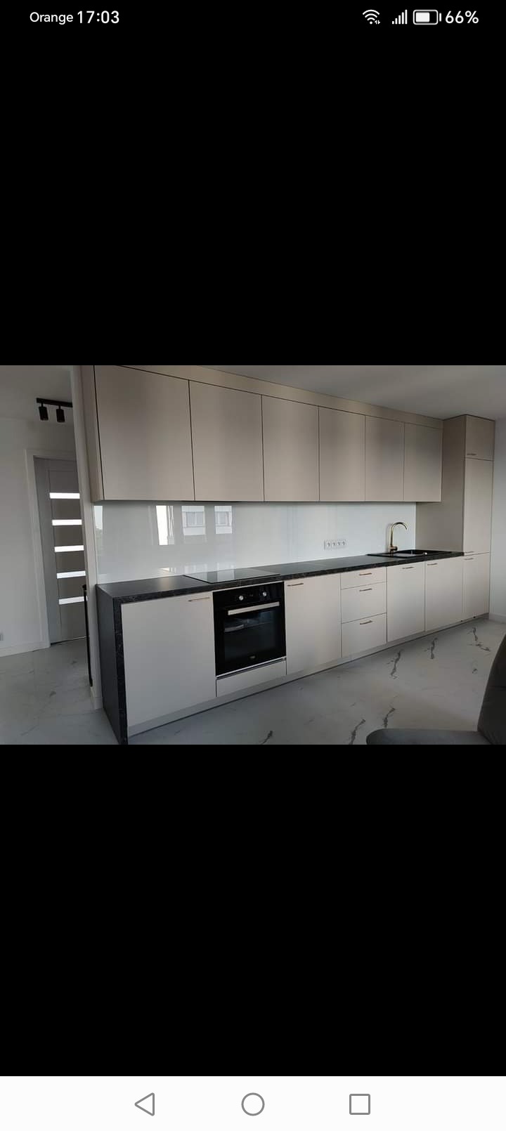 Nowoczesna kuchnia z beżowymi szafkami, czarnym blatem i białym lacobelem, widok na marmurową podłogę i drzwi z szybami.