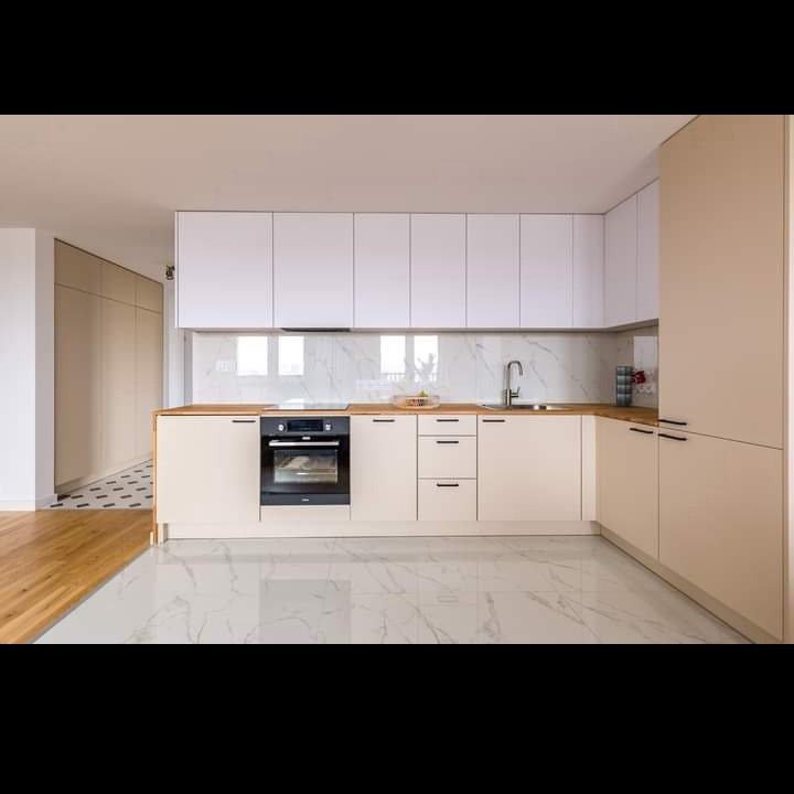 Jasna kuchnia z białymi górnymi szafkami i beżowymi dolnymi, blatem z jasnego drewna i marmurową podłogą, widok na fragment parkietu w sąsiednim pomieszczeniu.