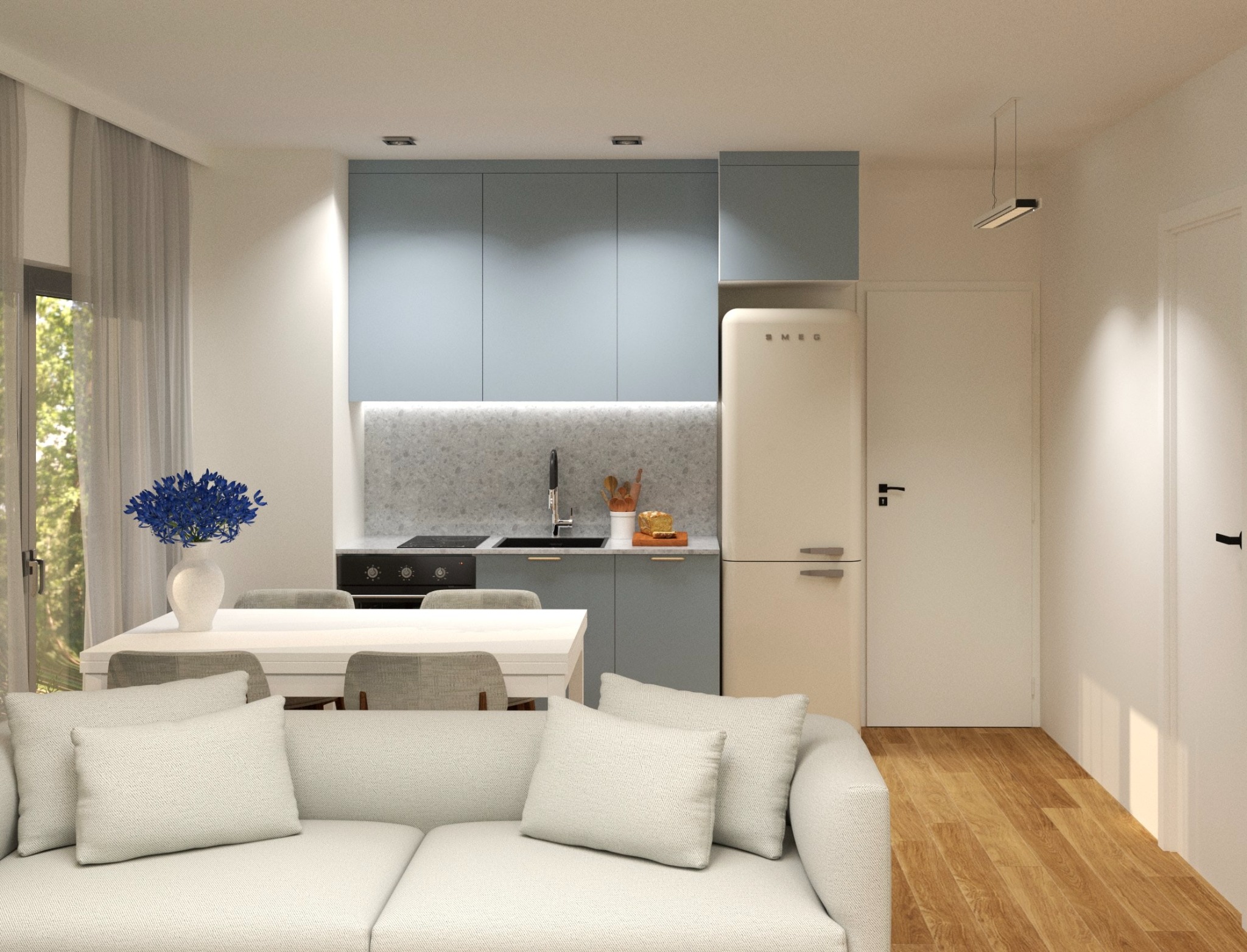 Jasne wnętrze z pastelową zabudową kuchenną, kremową lodówką retro Smeg i drewnianą podłogą. W tle okno z firaną, a na pierwszym planie biała sofa.