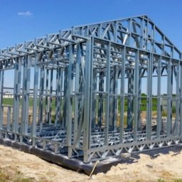 Global Invest development - Szkielet modułowego domu w konstrukcji stalowej, widoczne elementy nośne i montażowe na fundamencie z izolacją, jasne niebo w tle.