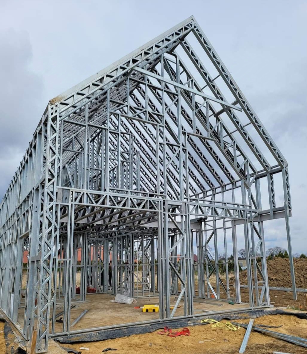 Konstrukcja szkieletowa domu z profili stalowych, widok z zewnątrz na placu budowy, z widocznymi elementami mocującymi i narzędziami wewnątrz.