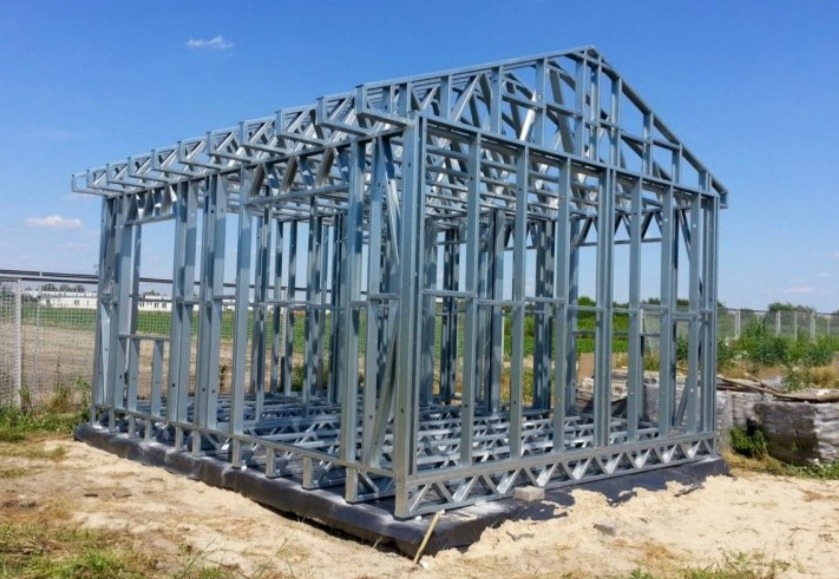 Szkielet modułowego domu w konstrukcji stalowej, widoczne elementy nośne i montażowe na fundamencie z izolacją, jasne niebo w tle.
