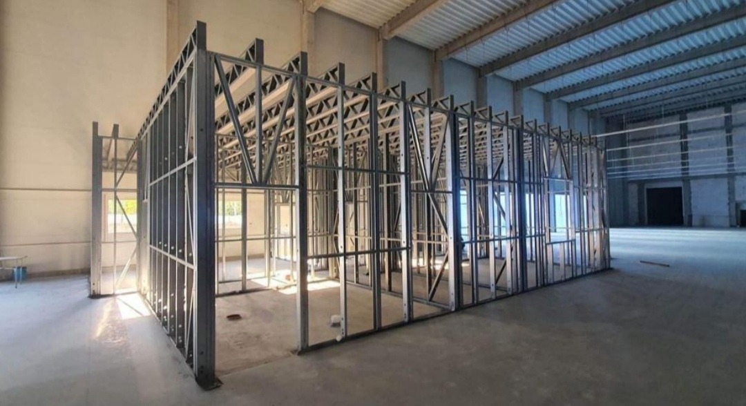 Metalowa konstrukcja szkieletowa wewnątrz hali, widoczne okna i elementy konstrukcyjne dachu, przygotowana pod zabudowę ścian.