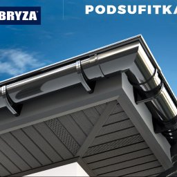 DACH-SYSTEM - Czarne, błyszczące rynny zamontowane na szarej podbitce dachowej, widok z dołu na tle błękitnego nieba.