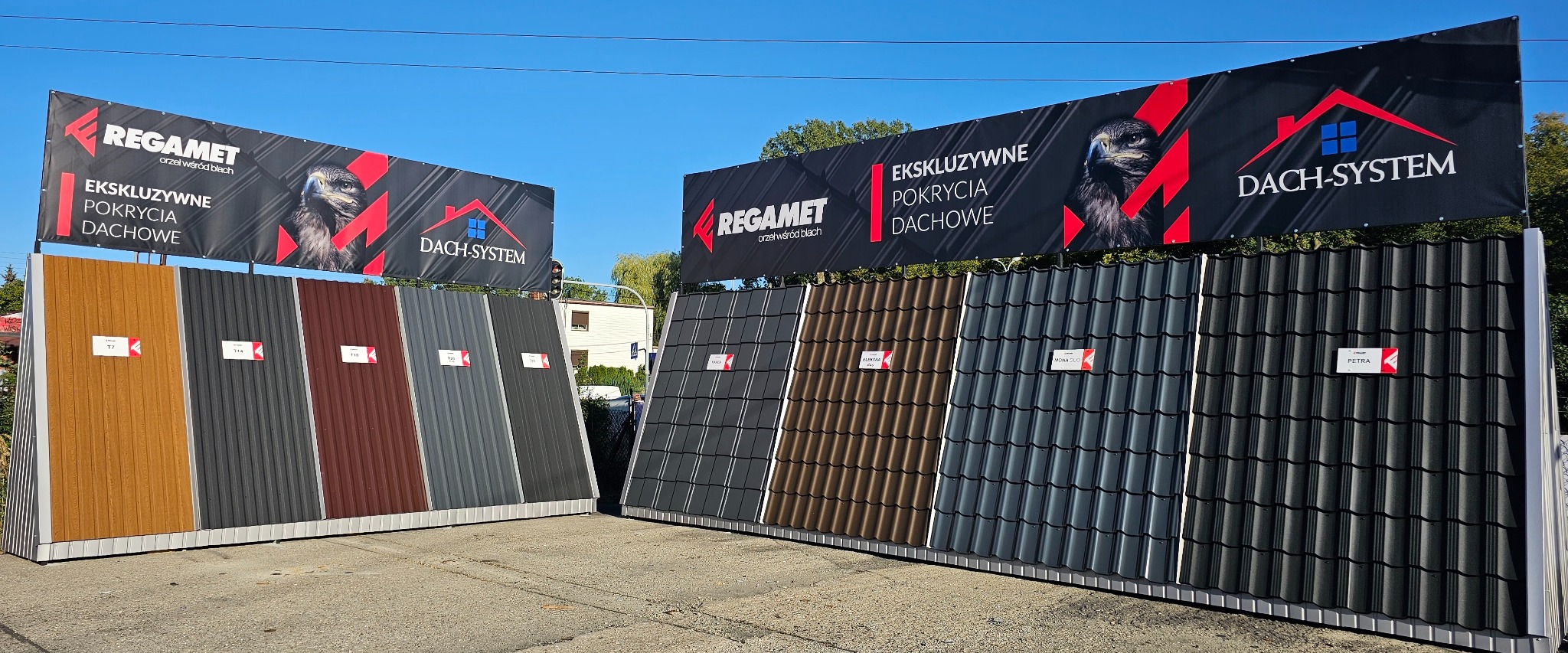 Ekspozycja próbek różnych kolorów i wzorów blaszanych pokryć dachowych marek Regamet i Dach-System na tle błękitnego nieba.