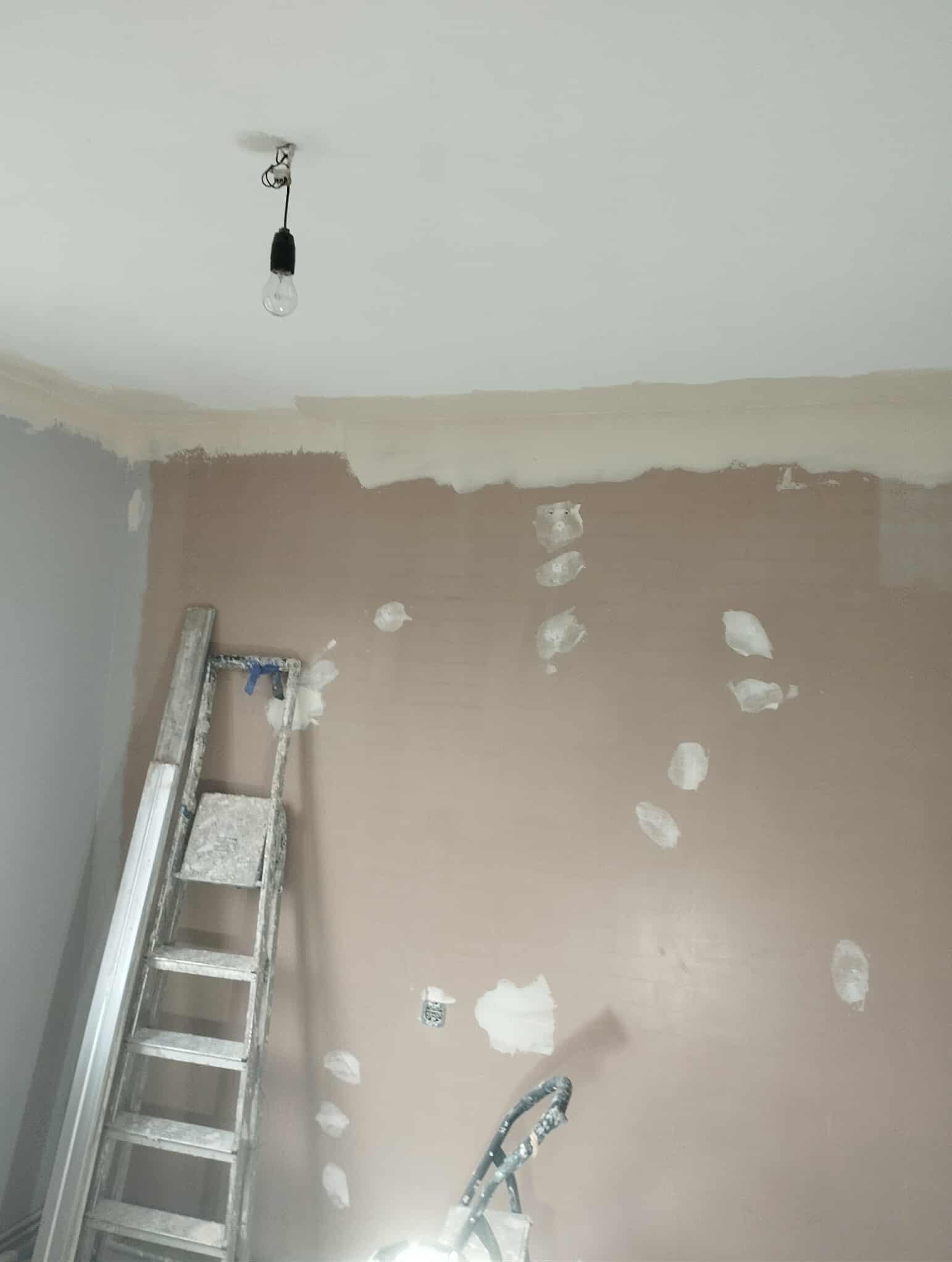 Ściana po szpachlowaniu z łatami i drabina w Trzciance. Przygotowanie do malowania, widoczne niedoskonałości i surowy stan wykończenia.