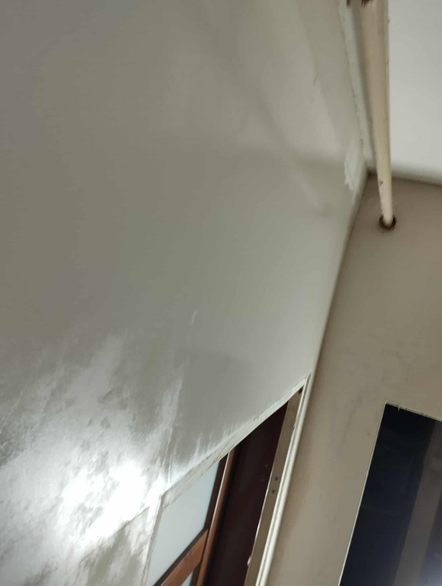 Świeżo położona, błyszcząca gładź na ścianie w trakcie remontu, widoczne ramy okienne i rura pod sufitem. Ujęcie pod kątem, podkreślające fakturę wykończenia.