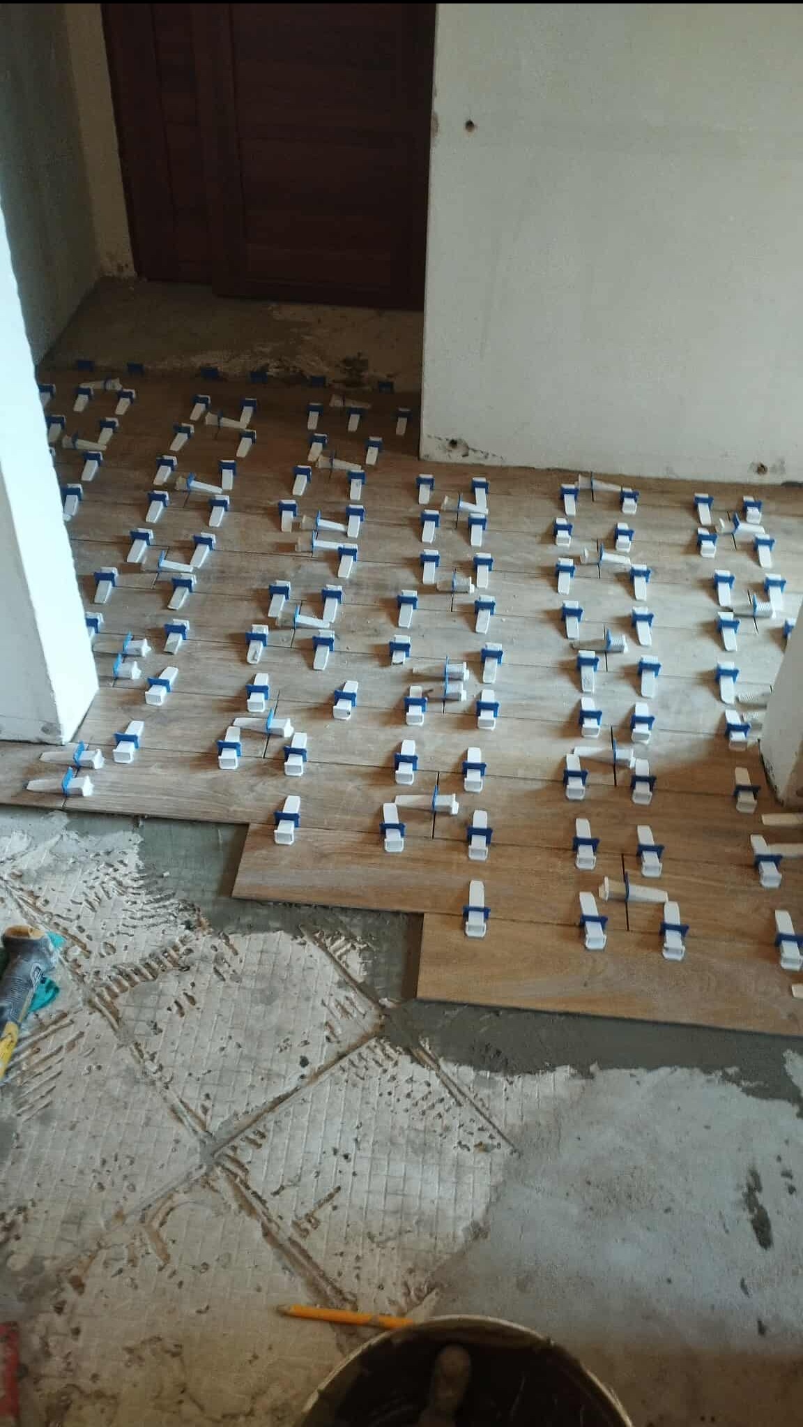 Układanie płytek podłogowych imitujących drewno, z użyciem klipsów poziomujących. Fragment widocznej, starej podłogi. Etap prac przed fugowaniem.