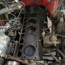 QuickService Mateusz Góra - Odsłonięty blok silnika z widocznymi cylindrami, zanieczyszczony olejem, w trakcie demontażu w warsztacie samochodowym.