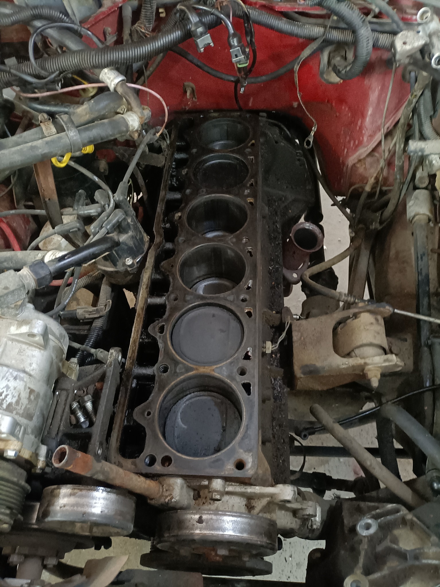 Odsłonięty blok silnika z widocznymi cylindrami, zanieczyszczony olejem, w trakcie demontażu w warsztacie samochodowym.