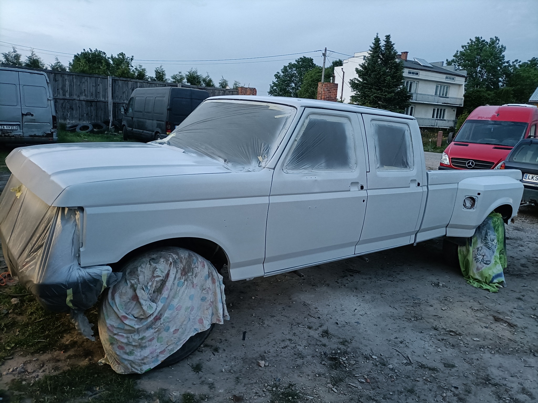 Biały pickup Ford F-350 po szpachlowaniu, przygotowany do lakierowania, z maskowaniem folią i materiałem, na zewnątrz warsztatu.